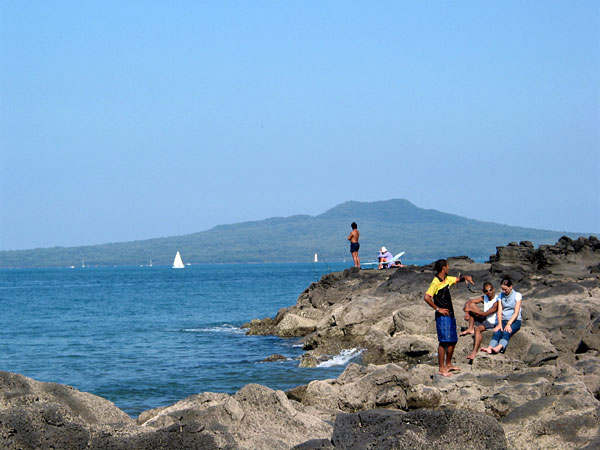 People and fishermen relaxing on the rocks by the sea, Rangitoto Island in background, Auckland, New Zealand